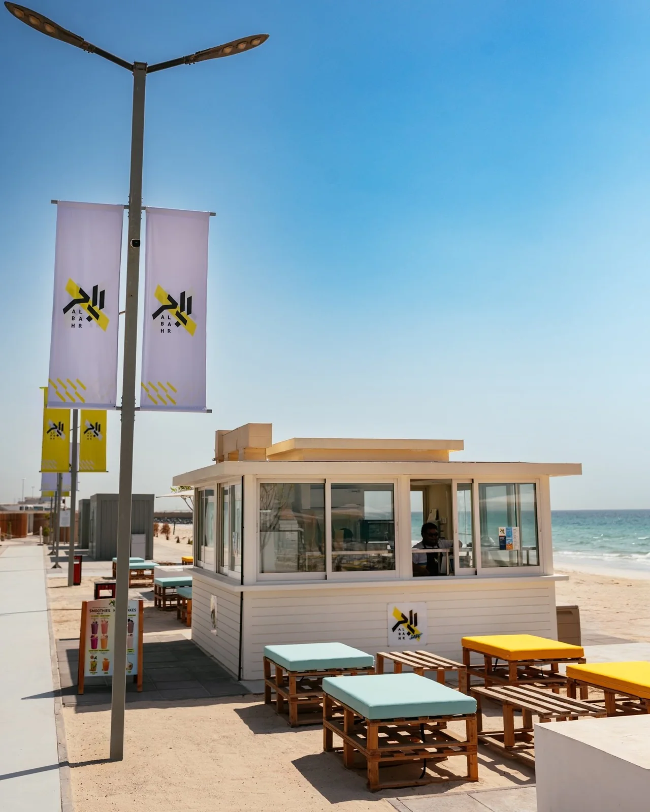 The white Al Bahr Café kiosk and colourful outdoor benches beneath a blue sky.
