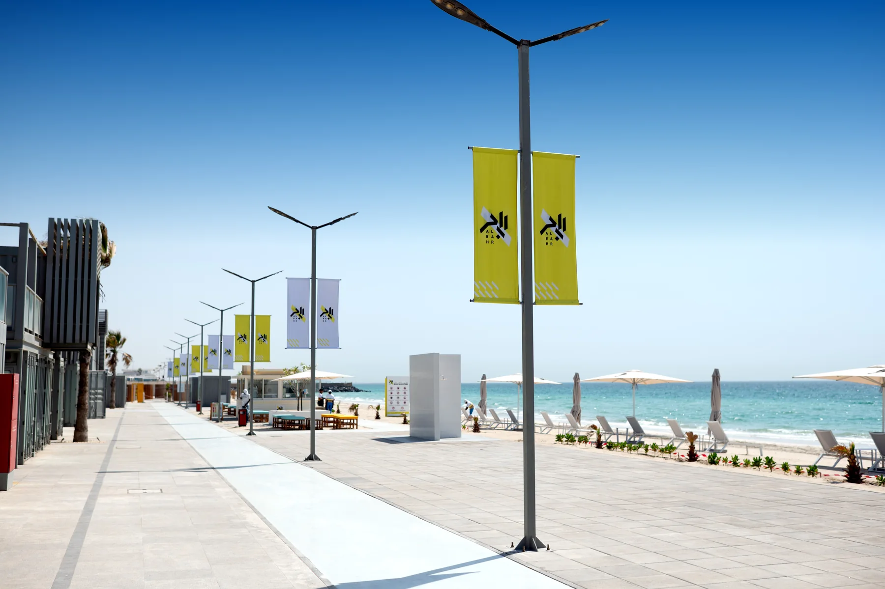 Al Bahr’s beachfront promenade with yellow flags and the sea beyond.