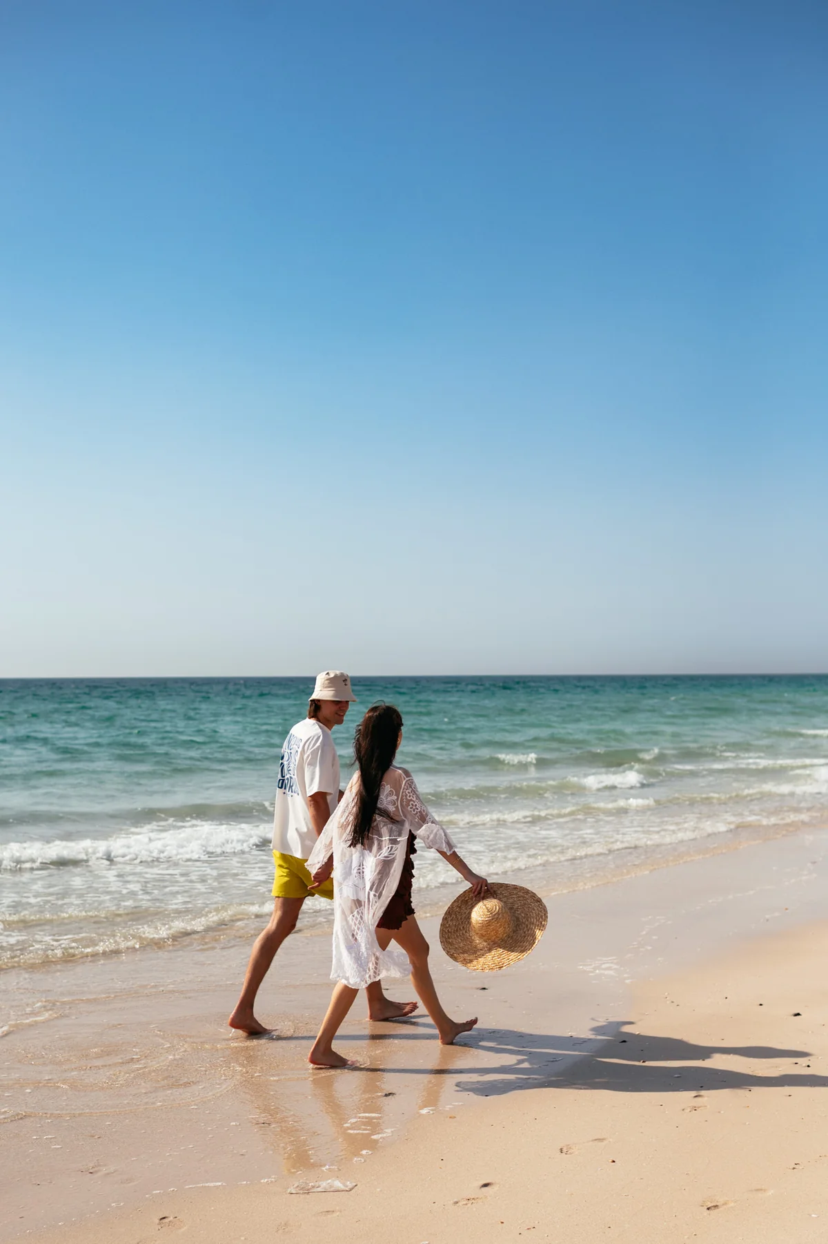 Two visitors walking along the water’s edge at Al Bahr Beach.